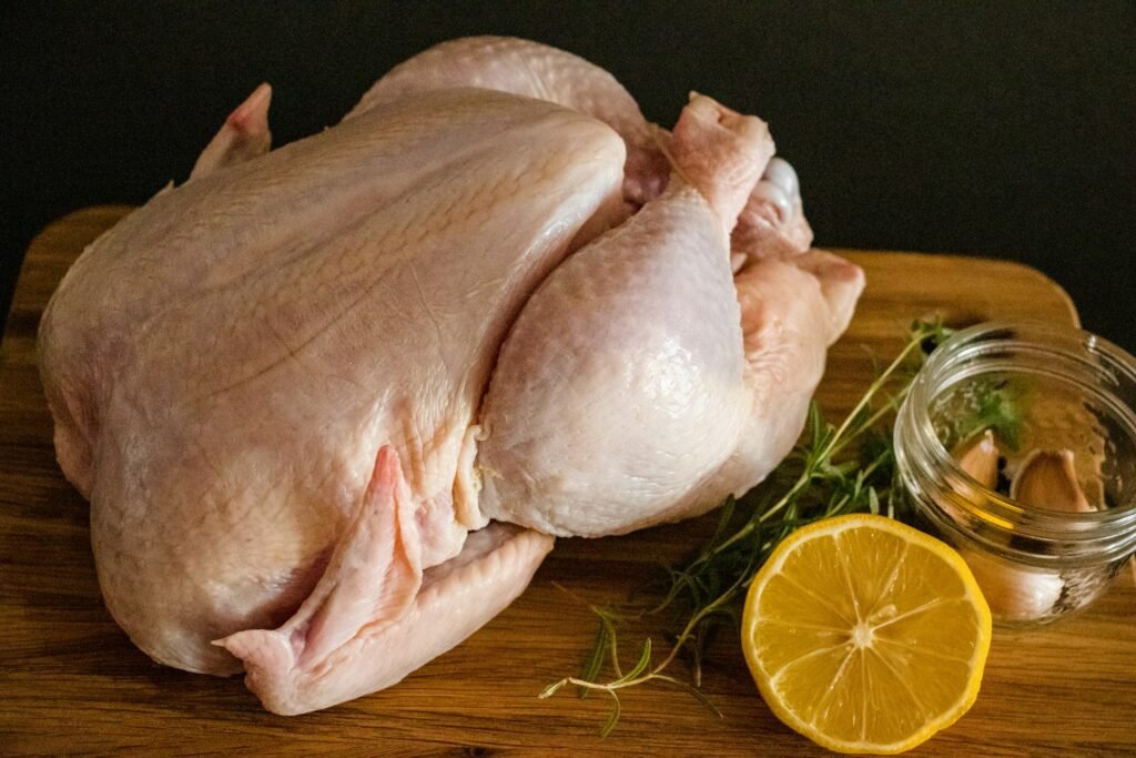 Pollo entero fresco sobre tabla de madera